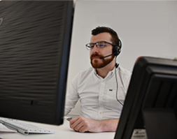 A man wearing a headset, looking at his desktop computer